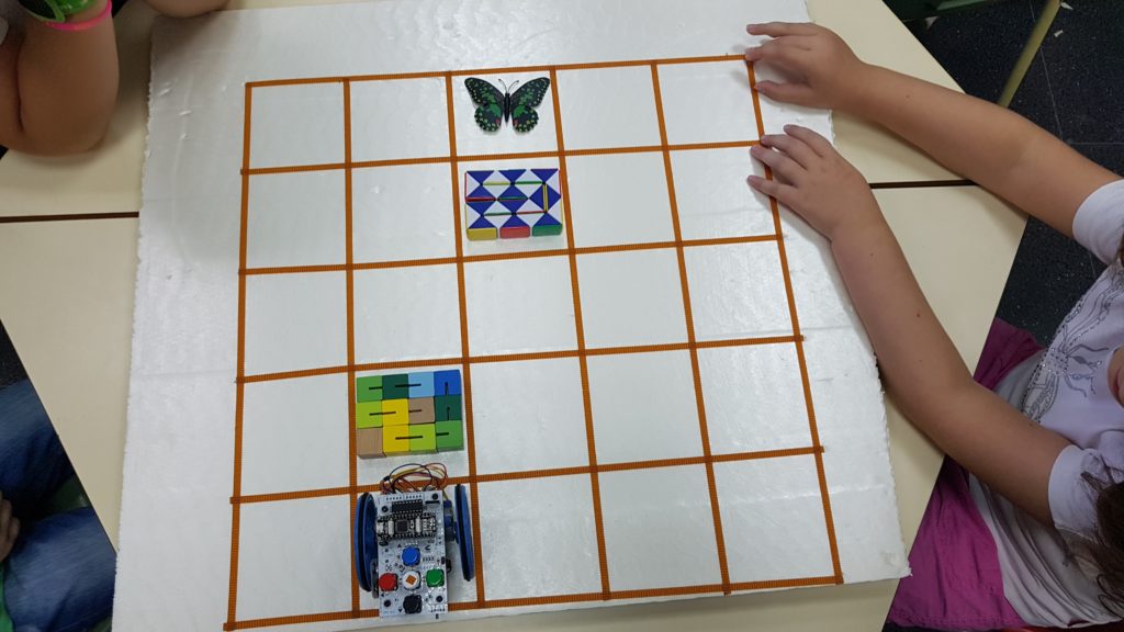 En la imagen se puede ver un robot Escornabot, una mariposa y dos objetos que ocupan dos celdas de un tablero de porexpan de 5x5 celdas