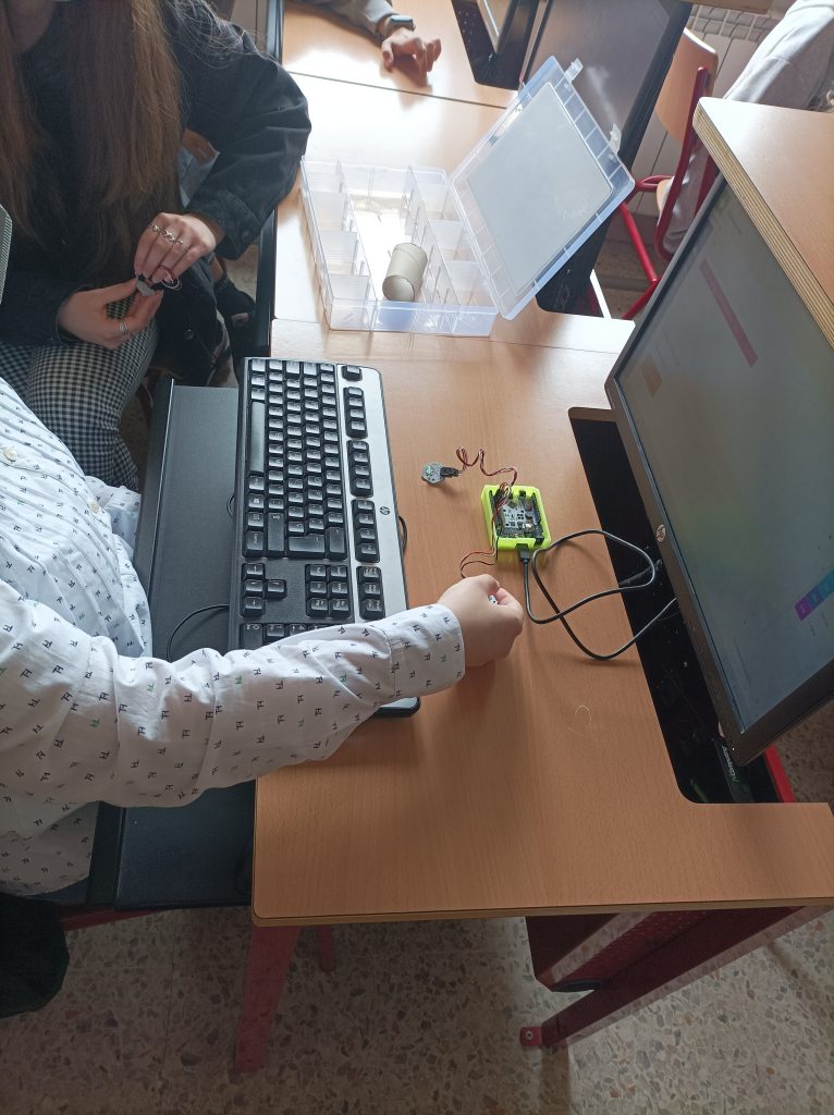 Alumnado interactuando con el ordenador y un pequeño robot.