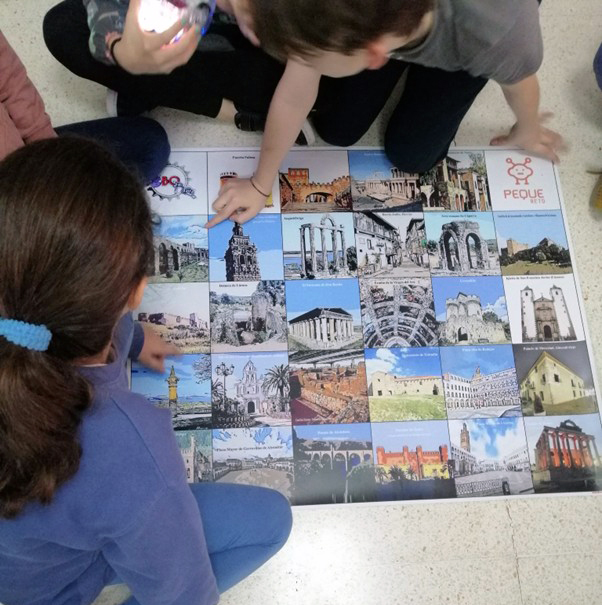 Varios alumnos y alumnas sobre un tablero de Blue Bot o Bee Bot con elementos arquitectónicos y culturales de España