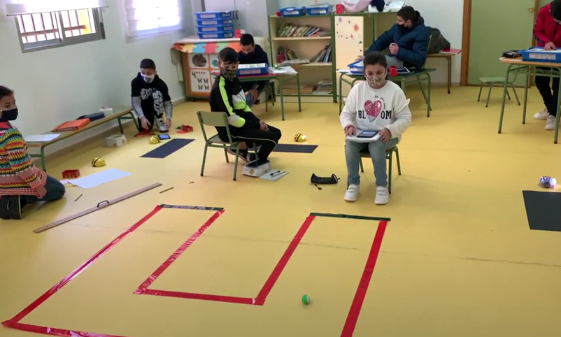 Circuito marcado con cinta aislante roja en el suelo. Una alumna, con su tablet, comprueba que el robot sigue correctamente el circuito.